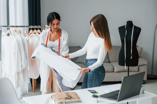 Talking with female customer. Seamstress is in her office that is with different clothes.