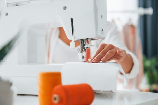 Working by using sewing machine. Seamstress is in her office that is with different clothes.