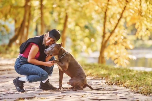 Having fun. Woman in casual clothes is with pit bull outdoors.