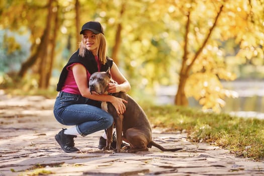 Having fun. Woman in casual clothes is with pit bull outdoors.
