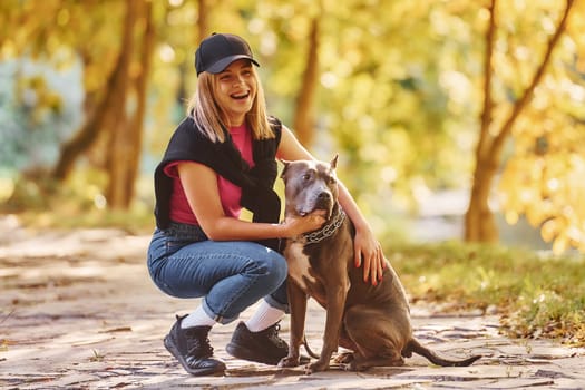 Having fun. Woman in casual clothes is with pit bull outdoors.