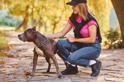 Yellow leaves at background. Woman in casual clothes is with pit bull outdoors.