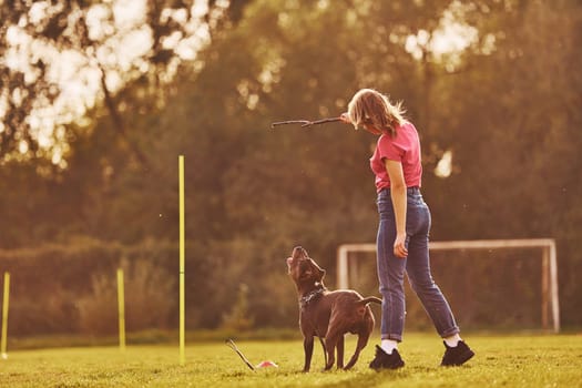 On sportive field. Woman in casual clothes is with pit bull outdoors.