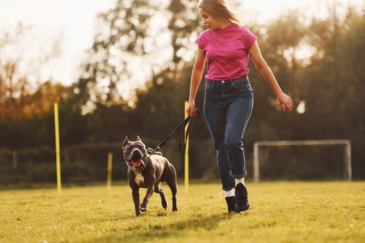 On sportive field. Woman in casual clothes is with pit bull outdoors.