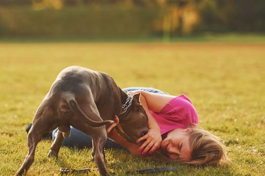 Playing on the ground. Woman in casual clothes is with pit bull outdoors.