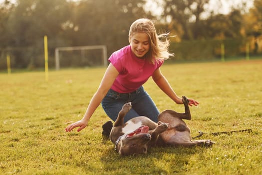 Playing on the ground. Woman in casual clothes is with pit bull outdoors.