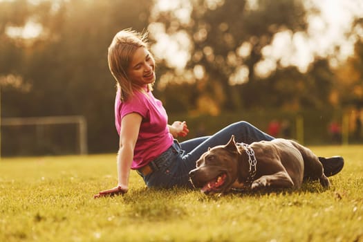 Playing on the ground. Woman in casual clothes is with pit bull outdoors.