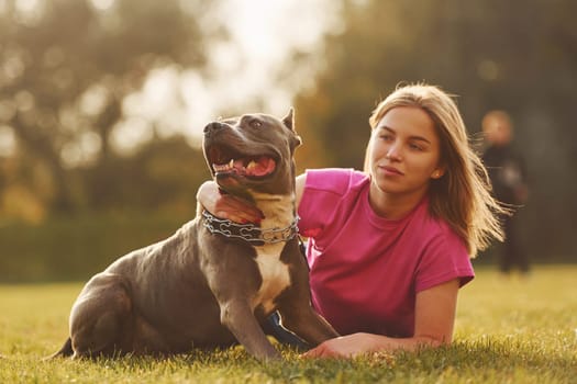 Laying down on the ground. Woman in casual clothes is with pit bull outdoors.