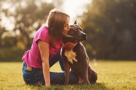 On the green grass. Woman in casual clothes is with pit bull outdoors.