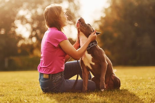 Embracing the dog. Woman in casual clothes is with pit bull outdoors.
