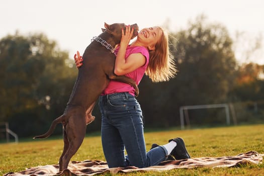 Friendship between human and animal. Woman in casual clothes is with pit bull outdoors.