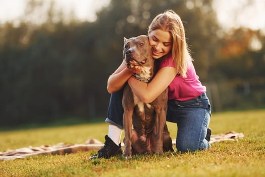 Friendship between human and animal. Woman in casual clothes is with pit bull outdoors.