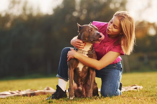 Friendship between human and animal. Woman in casual clothes is with pit bull outdoors.