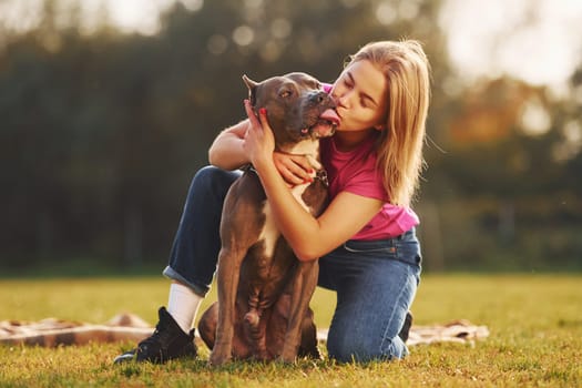 Positive emotions. Woman in casual clothes is with pit bull outdoors.