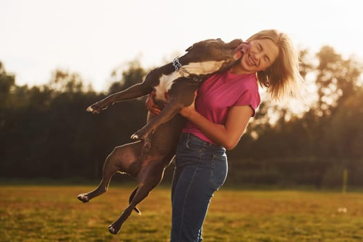 Outdoors on the field. Woman in casual clothes is with pit bull.