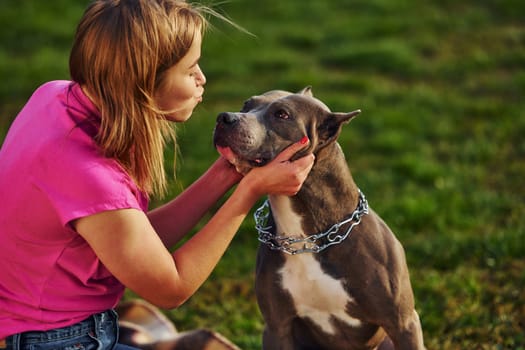 Outdoors on the field. Woman in casual clothes is with pit bull.