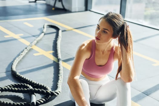 Sitting with rope. Beautiful young woman with slim body type is in the gym.