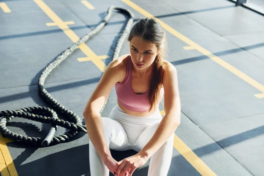 Sitting with rope. Beautiful young woman with slim body type is in the gym.
