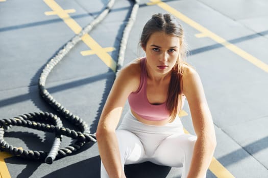 Sitting with rope. Beautiful young woman with slim body type is in the gym.
