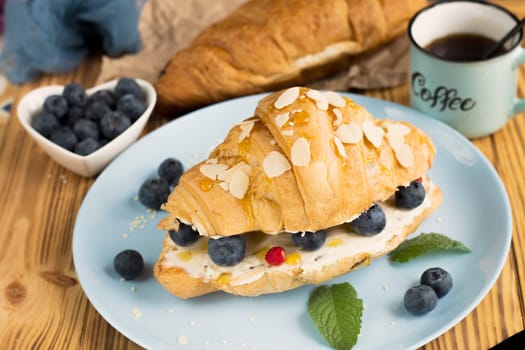 Croissant sandwich with cheese , arugula and berries. classic american breakfast. Fresh french croissant with fresh berries. blueberry and strawberry on cream cheese. Croissant and a cup with coffee