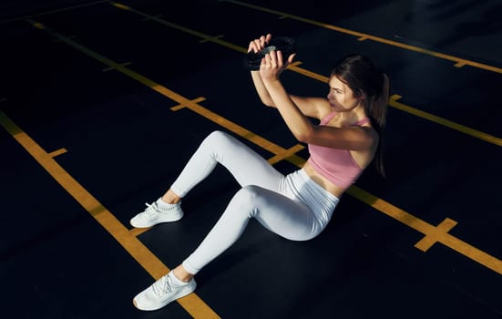 Holding weight in hands. Beautiful young woman with slim body type is in the gym.