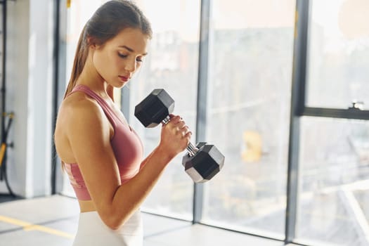 Standing with equipment. Beautiful young woman with slim body type is in the gym.