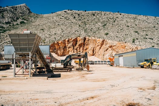 Heavy duty screen excavator with dump trucks in the background. Quarry mining machinery equipment. Crushing and screening