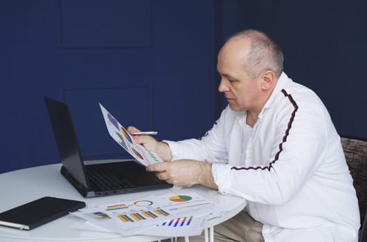 Male businessman works on laptops, studies reporting documents, charts and graphs.