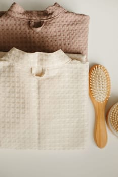 On a white surface are two bathrobes, a comb and a washcloth. Close-up
