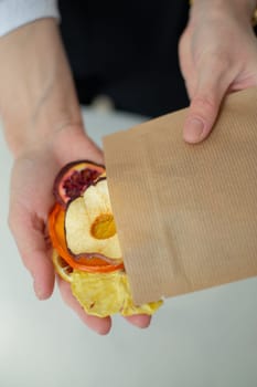 In the hands of a woman is a paper bag with candied fruits. Close-up.