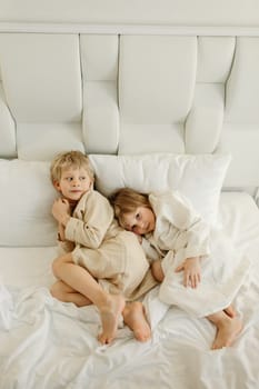 Brother and sister lying on the bed in bathrobes after a shower.