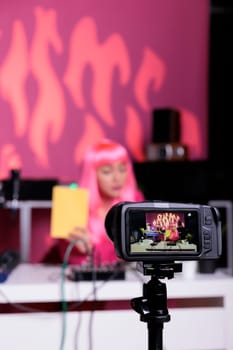 Influencer holding notebook showing product in front of camera while recording review using professional vlogging equipment. Asian content creator standing at desk filming vlog in broadcast studio