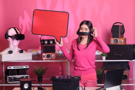 Smiling artist holding red speech bubble advertising text messages cardboard in studio over pink background. Asian musician playing sounds to produce melody at professional mixer console