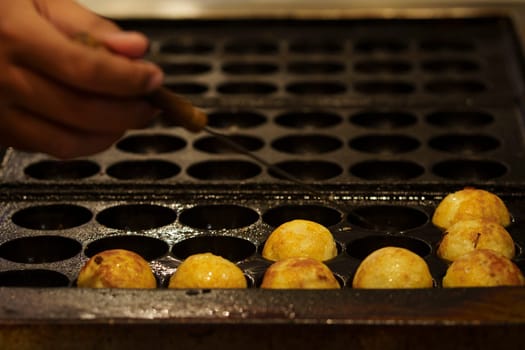 The cooking of Takoyaki. The popular Japanese street food that consists of small, ball-shaped snacks made of batter and filled with small pieces of octopus and other ingredients.
