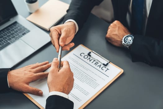 Two businesspeople sit across the desk as business deal is taking place. Corporate attorney giving a pen for client or partner to sign contract paper, sealing the deal with signature. Fervent