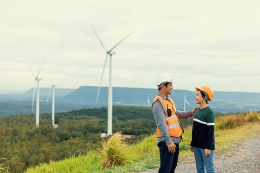 Engineer with his son on a wind farm atop a hill or mountain in the rural. Progressive ideal for the future production of renewable, sustainable energy. Energy generation from wind turbine.