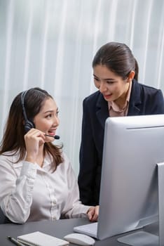 Asian female customer support operator wearing headset is guided by her supportive manager. Experienced colleague help operator handle a call with a client, providing advice and guidance. Enthusiastic