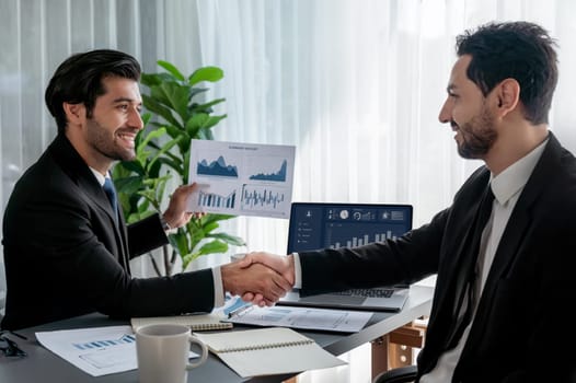 Closeup professional businessman shaking hands over desk in modern office after successfully analyzing pile of dashboard data paper as teamwork and integrity handshake in workplace concept. fervent