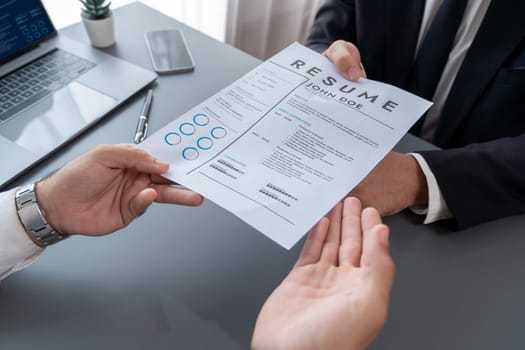 Confident man wearing suit in formal office, hand holding resume paper during job interview. Interviewer asking questions, evaluating candidate qualification and suitability for job position. Fervent