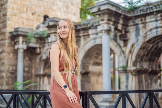Happy female tourist traveler discover interesting places and popular attractions and walks in the old city of Antalya. Hadrian Kapisi turkey landmark city history. Popular tourist attraction - ancient Roman Hadrian Gate in old town Antalya, Turkey on a summer day. Turkiye.