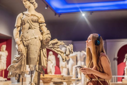 Portrait of contemporary young woman looking at sculptures and listening to audio guide at museum exhibition.