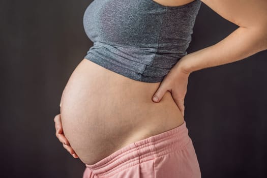 Lower back pain, discomfort during pregnancy on a dark background.