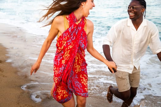 Young multiracial happy couple running along seaside during vacation travel holding hands. Romance concept.