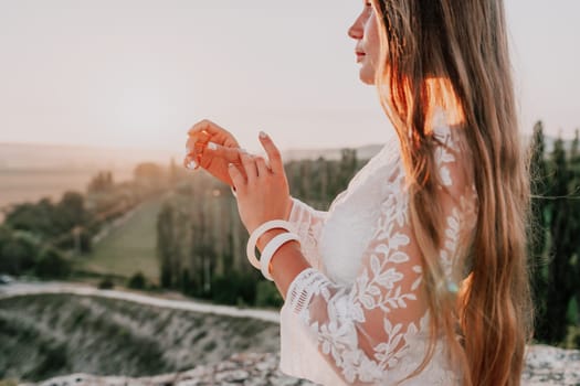 Romantic beautiful bride in white dress posing with sea and mountains in background. Stylish bride standing back on beautiful landscape of sea and mountains on sunset