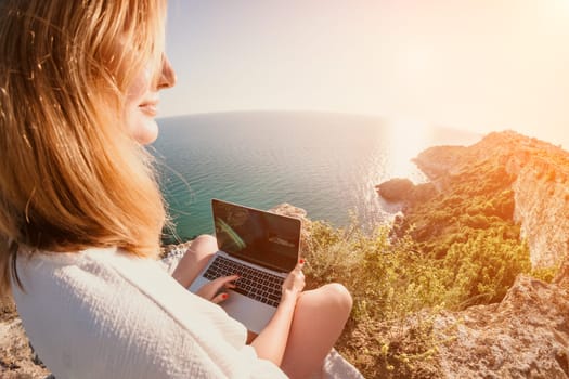 Woman sea laptop. Business woman in yellow hat working on laptop by sea. Close up on hands of pretty lady typing on computer outdoors summer day. Freelance, digital nomad, travel and holidays concept.