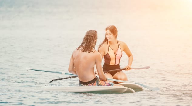 Sea woman and man on sup. Silhouette of happy young woman and man, surfing on SUP board, confident paddling through water surface. Idyllic sunset. Active lifestyle at sea or river