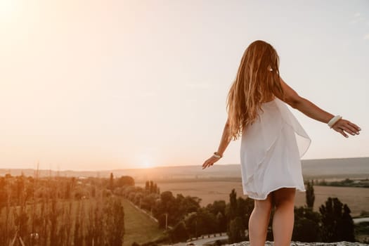 Romantic beautiful bride in white dress posing with sea and mountains in background. Stylish bride standing back on beautiful landscape of sea and mountains on sunset