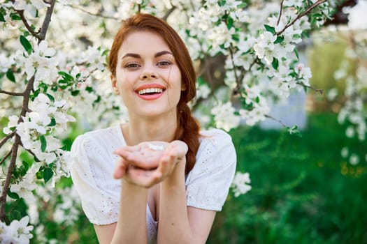 portrait of a beautiful red-haired woman against the background of a flowering tree with flowers in her palms. High quality photo