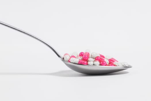 Spoon with pink pills on a white background. Drug overuse and antibiotic resistance.