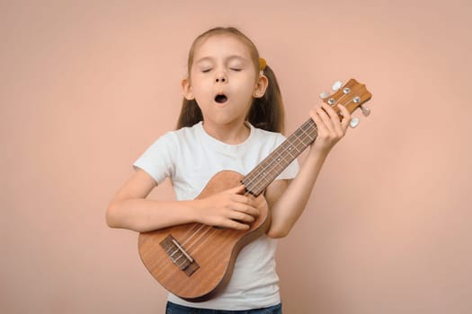 Caucasian preschool girl learning to sing by playing the ukulele.